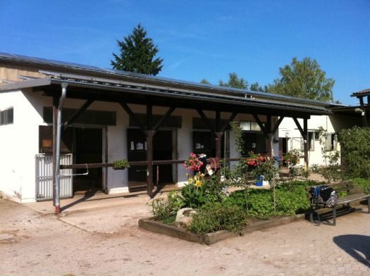 Stallgebäude mit überdachtem Vorplatz und Blumenbeet